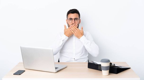 Jonge zakenman op een werkplek die mond met handen bedekt - Foto, afbeelding