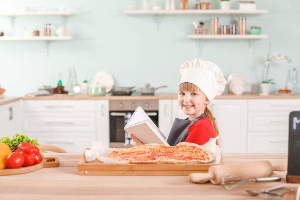 Cute little chef z książki kucharskiej i pizzy w kuchni - Zdjęcie, obraz