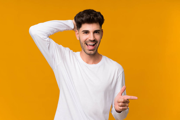 Young man over isolated orange background surprised and pointing finger to the side - 写真・画像