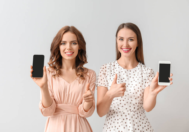 Junge Frauen mit Mobiltelefonen auf hellem Hintergrund - Foto, Bild