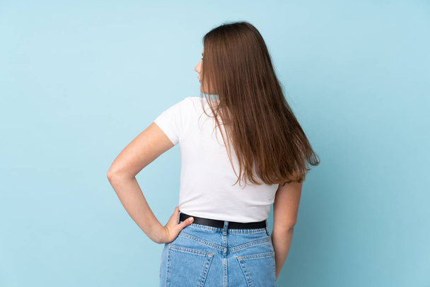 Teenager caucasian girl isolated on blue background in back position and looking side - Zdjęcie, obraz