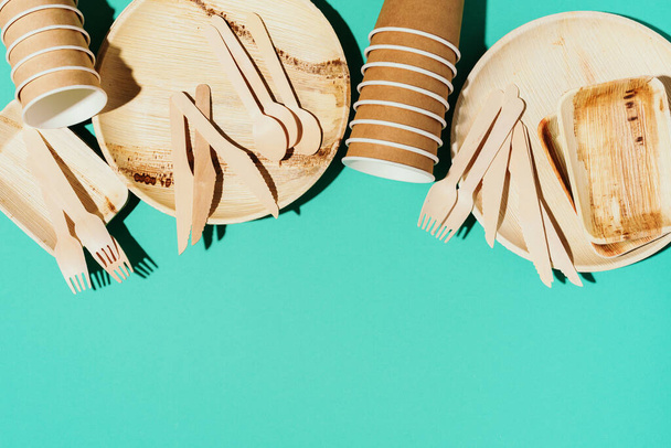 Disposable tableware from natural materials. Bamboo plates, wooden spoon, fork, knife, craft paper cups on blue background. Eco-friendly sustainable lifestyle. Eco-friendly disposable utensils - 写真・画像