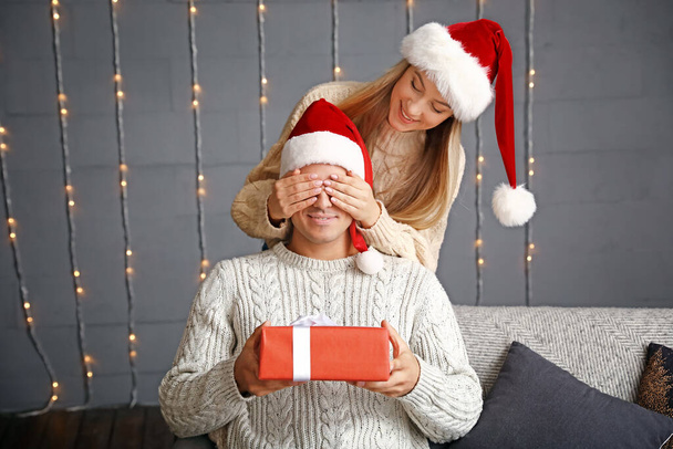 Femme heureuse couvrant les yeux de son mari avec un cadeau à la maison
 - Photo, image