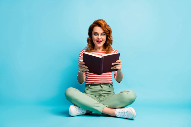 Full length photo of crazy book worm woman sit floor rest relax cross legs read book impressed scream wow omg wear white green footwear pants isolated blue color background - Φωτογραφία, εικόνα