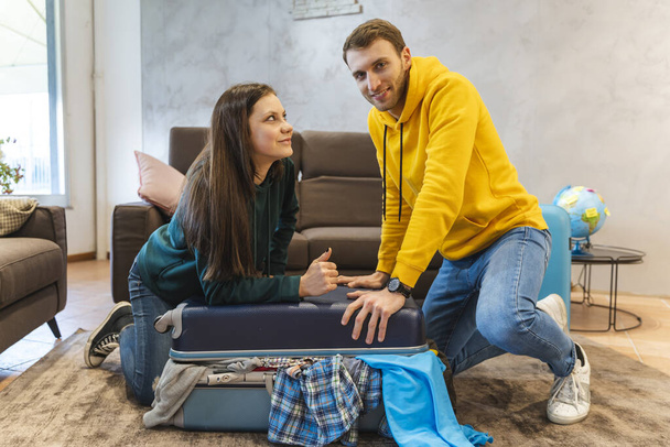young couple is preparing the suitcases for the next trip in the living room at home. holidays around the world concept - Фото, зображення