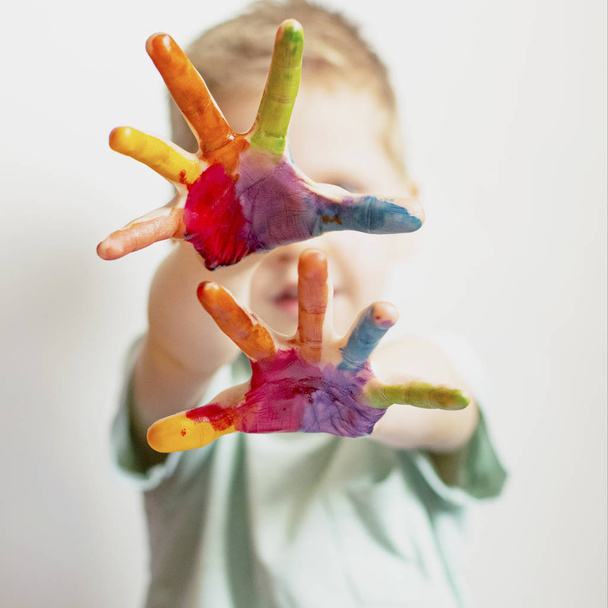 The child paints. Palms and hands of a child in multi-colored watercolor. Watercolor, gouache, paint brushes, colored and wax crayons, stickers. Set for drawing, creativity and hobbies - Foto, Bild