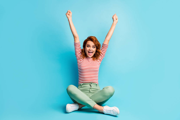 Full size photo of delighted woman sit legs crossed win fortune lottery raise fists scream yeah wear trendy sneakers isolated over blue color background - Foto, Imagem