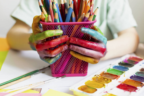 子供は絵を描く。多色の水彩画で子供の手のひらと手。水彩、ガッシュ、ペイントブラシ、色とワックスクレヨン、ステッカー。描画、創造性と趣味のためのセット - 写真・画像