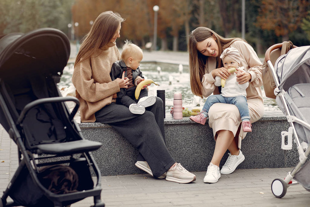 Two young mothers sitting in a autumn park with carriages - Fotoğraf, Görsel