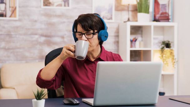 Old woman enjoying a cup of coffee while working on laptop - Photo, Image