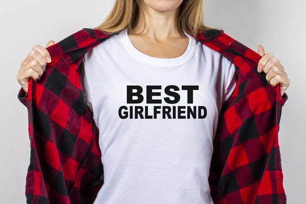 Jonge vrouw in een rood shirt en wit t-shirt op een witte achtergrond. T-shirt sms toegevoegd Beste vriendin. Concept voor tekst, logo, shock, verrassing. Banner. - Foto, afbeelding