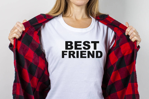Młoda kobieta z uśmiechem w czerwonej koszuli i białej koszulce na białym tle. T-shirt Best Friend dodał tekst. Koncepcja przyjaciela, szok, niespodzianka. Sztandar. - Zdjęcie, obraz