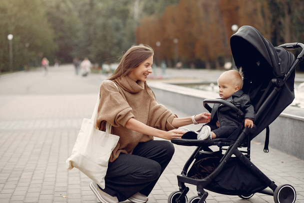 Young mother walking in a autumn park with carriage - Foto, afbeelding