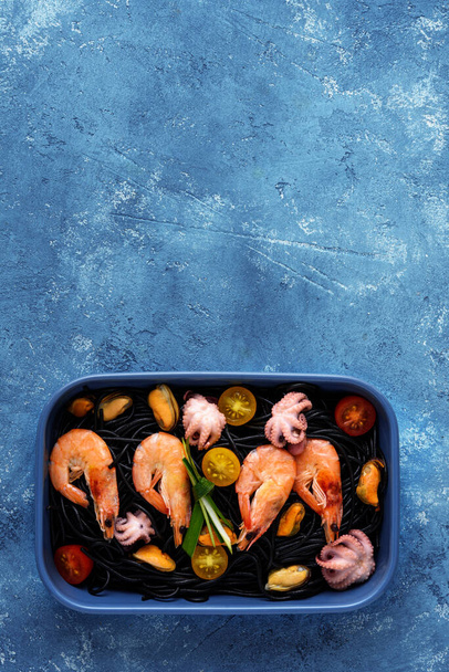 θαλασσινά με μαύρο σπαγγέτι σε μπλε πιάτο σε μπλε φόντο με αντίγραφο χώρου - Φωτογραφία, εικόνα