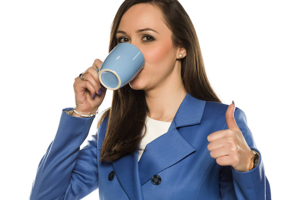 Young business woman drink from a mug on white background and showing thumbs u - Φωτογραφία, εικόνα