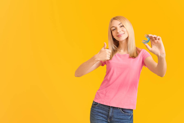 Junge Frau mit Zahnspange und Mundschutz zeigt Daumen-hoch-Geste auf farbigem Hintergrund - Foto, Bild