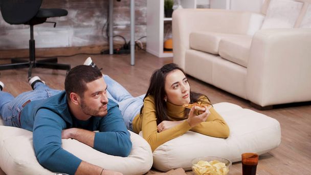 Genç bir adam ve bir kadın yerde uzanmış televizyon seyrediyor. - Fotoğraf, Görsel