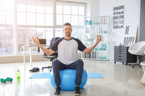 Man mediteren op fitness bal in het kantoor - Foto, afbeelding