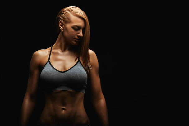 Portrait of a fit young woman posing wearing a sports bra against black background. Determined athlete in the studio. Copy space, black background, sports banner. - Photo, Image