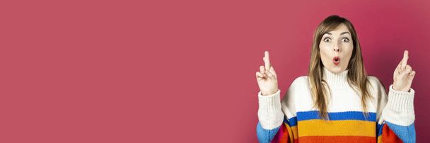 young girl in a knitted sweater shows a gesture of hands, crossed fingers for luck, luck on a burgundy background. Banner. - Photo, Image