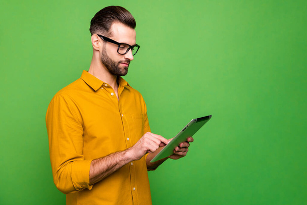 Profile side view portrait of nice attractive focused content guy in formal shirt holding in hand using digital tablet 5g connection isolated on bright vivid shine vibrant green color background - Foto, imagen