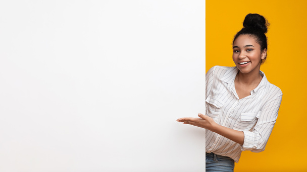 Mujer afro sonriente señalando el tablero de anuncios en blanco con la mano abierta
 - Foto, imagen