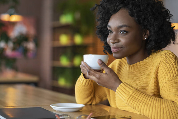 Jeune femme africaine rêveuse se détendant au café, buvant du café
 - Photo, image