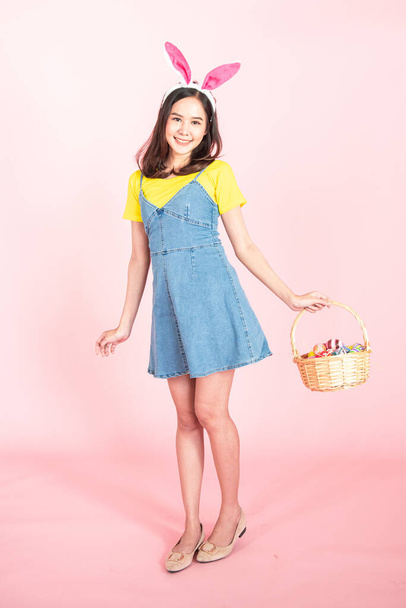full length studio shot of asian beauty happy young woman wearing bunny ears and holding colorful Easter egg in wood basket with lovely smile and colorful decor costume isolated on pastel backgrounds. - Foto, Imagen