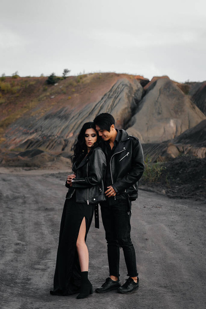 An Asian couple in love in black leather clothes walk in nature among the trees. Style, fashion, love - Foto, Imagem