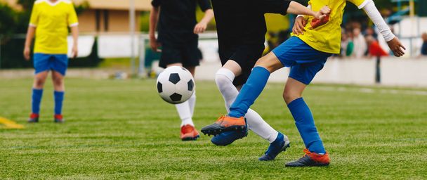 ジュニアサッカーの試合。少年たち草の上にサッカーの試合をキックスポーツフィールド.黄色と黒のジャージーシャツの若い選手の間のサッカーデュエル - 写真・画像