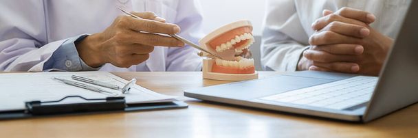 Fogorvos bemutatja és elmagyarázza a betegnek a fogbetegség kezelését fogászati műfogsor és feltáró tükör segítségével a fogászati klinika irodájában. Egészségügyi koncepció. - Fotó, kép