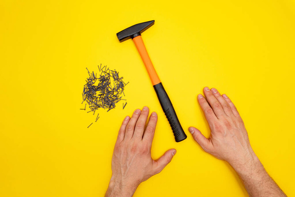 Hammer, male hands and pile of nails on yellow background - 写真・画像