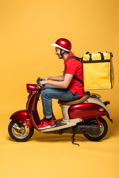 side view of delivery man with backpack on scooter on yellow background - Foto, immagini