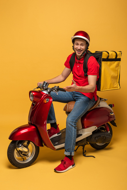 happy delivery man with backpack on scooter on yellow background - Fotoğraf, Görsel