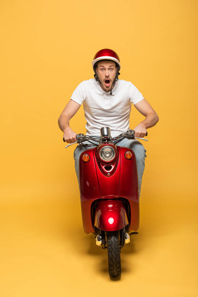 shocked delivery man in helmet riding scooter on yellow background - Photo, image