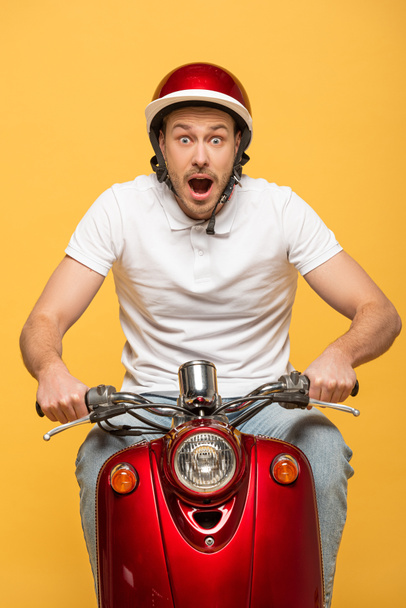 shocked delivery man in helmet riding scooter isolated on yellow - Foto, imagen