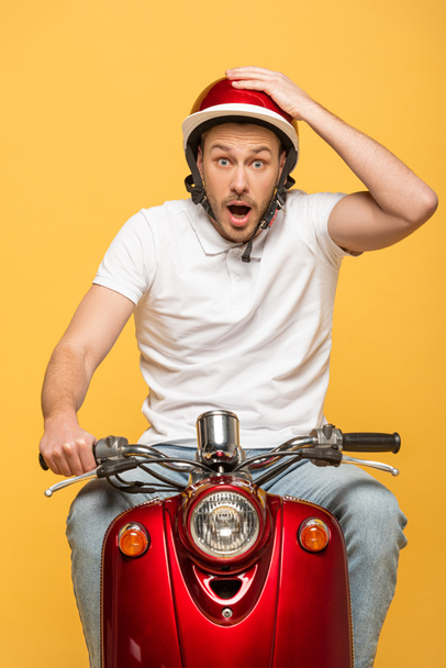 shocked delivery man in helmet riding scooter isolated on yellow - 写真・画像