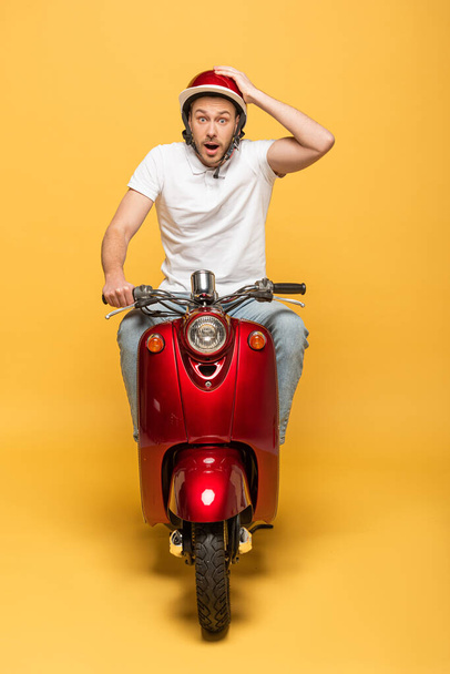 shocked delivery man in helmet riding scooter on yellow background - Foto, Bild