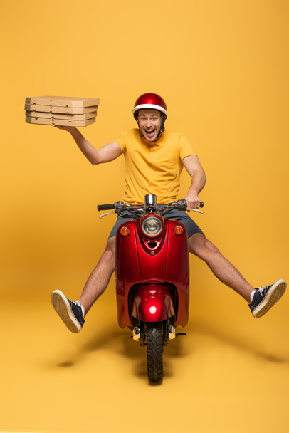 homem de entrega feliz em amarelo uniforme equitação scooter com caixas de pizza no fundo amarelo
 - Foto, Imagem