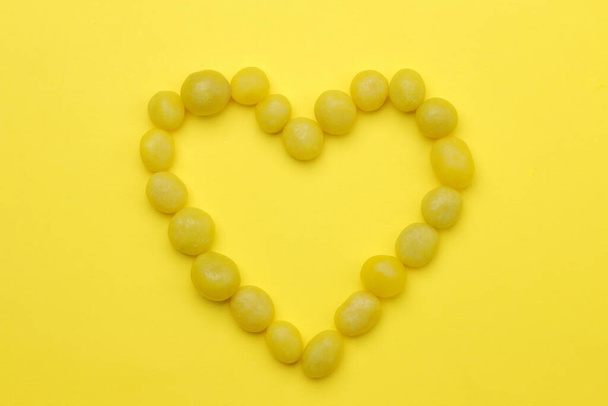 O conceito de minimalismo. Coração feito de doces amarelos doces em um fundo amarelo brilhante. vista superior
. - Foto, Imagem