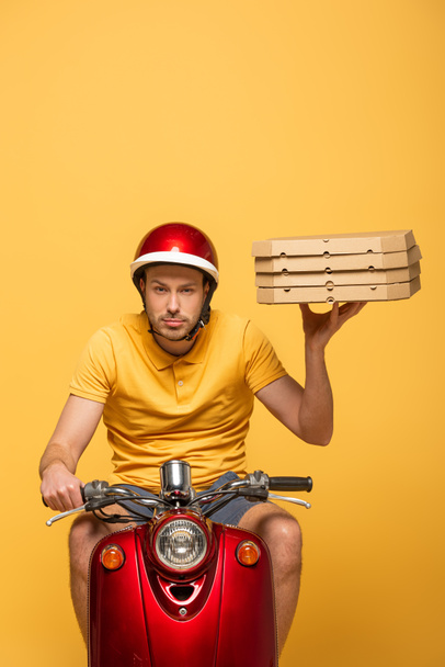 concentrated delivery man in yellow uniform riding scooter with pizza boxes isolated on yellow - Foto, Imagem