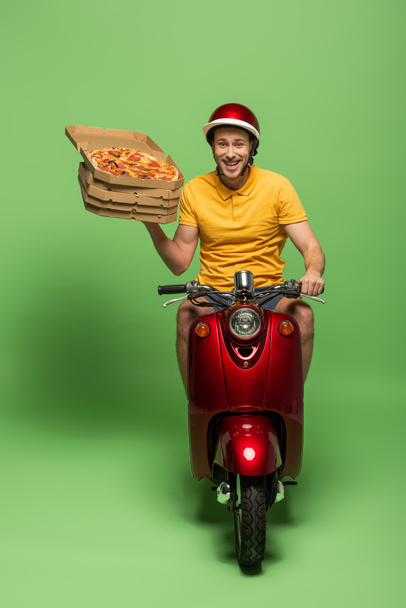 Zusteller in gelber Uniform auf Roller, der Pizza auf Grün liefert - Foto, Bild
