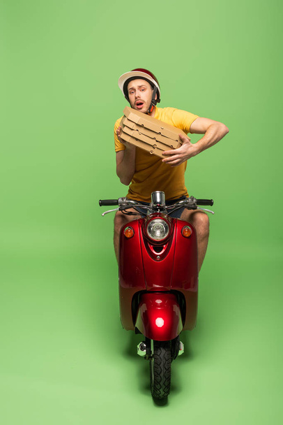 worried delivery man in yellow uniform on scooter with pizza boxes on green - Foto, Imagen
