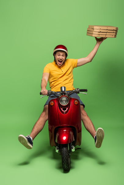 mad delivery man in geel uniform op scooter leveren pizza op groen - Foto, afbeelding