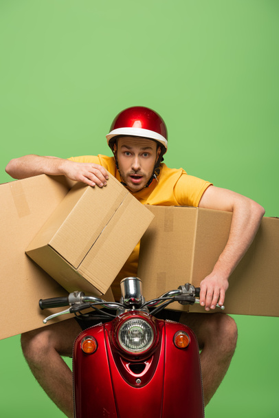 mad delivery man in yellow uniform on scooter with boxes isolated on green - 写真・画像