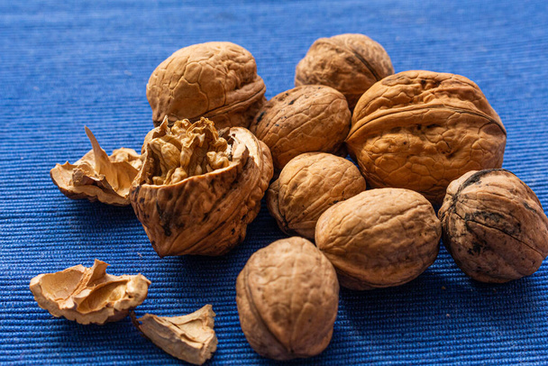Close up at seed of Walnut (Juglans regia) and uncraked in wooden bowl on blue background. Favorite for snack and very delicious. Have a lot of omega 3 for brain. Healthy food concept. - Photo, Image
