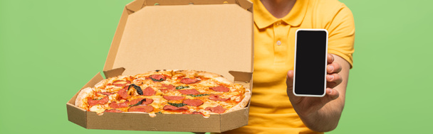 vista ritagliata di fattorino in uniforme gialla con pizza e smartphone isolato sul green, scatto panoramico
 - Foto, immagini