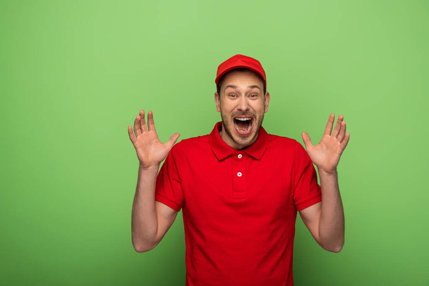 excited delivery man in red uniform showing hands on green - Foto, Imagem