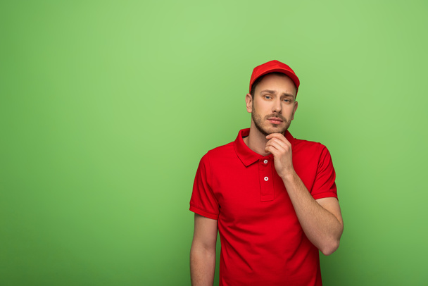 Nachdenklicher Zusteller in roter Uniform auf grünem Grund - Foto, Bild