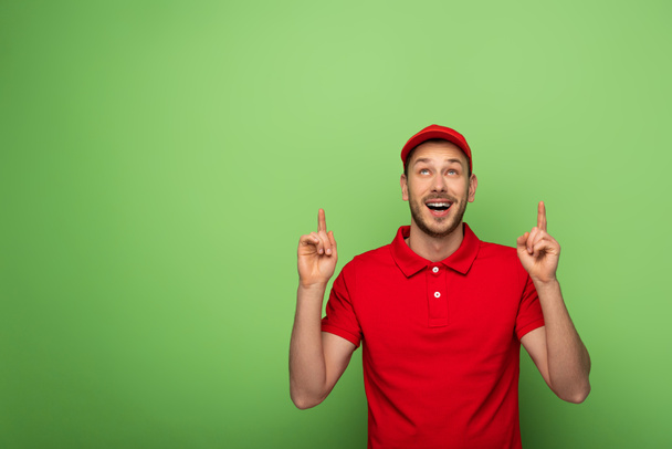 delivery man in red uniform pointing with fingers up on green - Photo, image